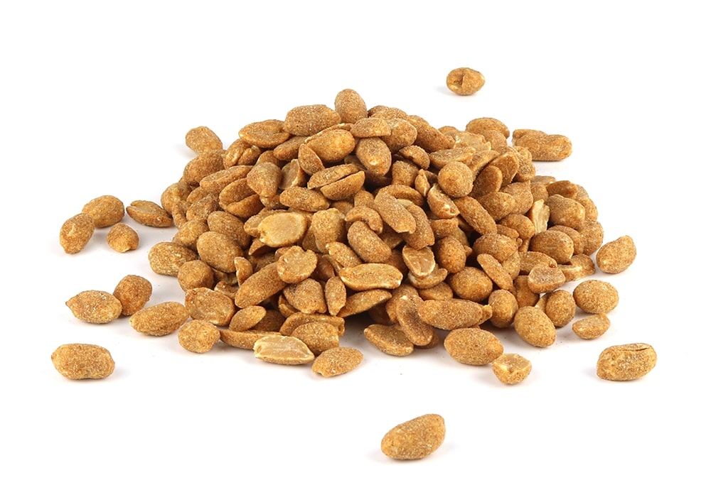 A heap of dry roasted peanuts is piled on a white surface, with some peanuts scattered around the main pile. The peanuts have a golden-brown coating, giving them a slightly sugary and crunchy appearance.